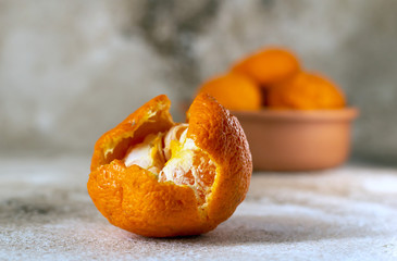 Partially peeled mandarin, whole mandarins on a table.