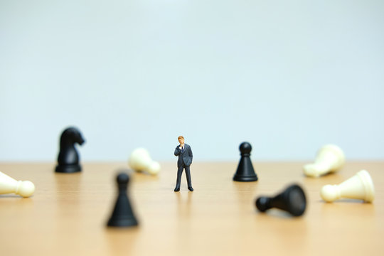 Business strategy conceptual photo - Miniature of businessman standing in the middle of collapsing chess pawn