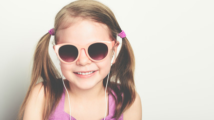 little happy girl in sunglasses and with headphones laughing - studio shot - copy space