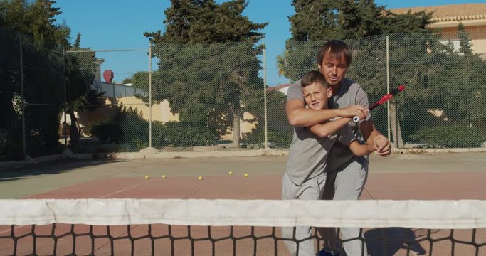Child traning in tennis. Father and son practice blows in tennis on coart. Active leisure together.