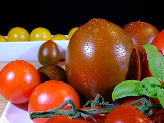 variants of tomatoes and raw beetroot, covered with fresh water drops, in front of a dark background