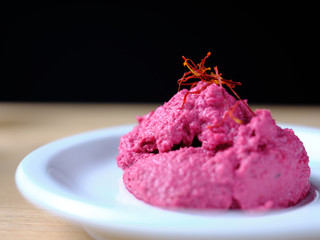 Horseradish with beetroot mousse, decorated with saffron threads, on a white plate arranged on a wooden shelve with dark background