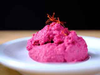 Horseradish with beetroot mousse, decorated with saffron threads, on a white plate arranged on a wooden shelve with dark background