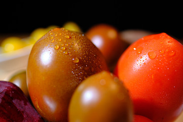Close up of variants of tomatoes and raw beetroot, covered with fresh water drops, in front of a dark background