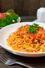 Spaghetti pasta with tomato sauce and parsley in white dish on black wooden table.
