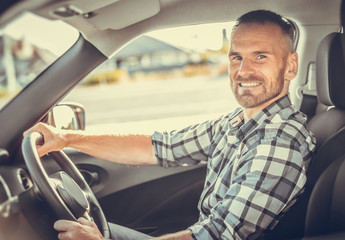 Attractive man driving a white car on a clear day. Buying or renting a car. Toned photo.