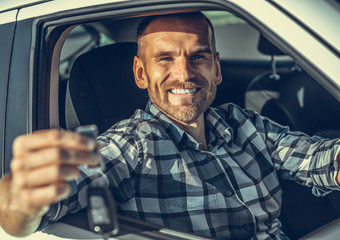 A male driver stands near a white car with a key in his hand and smiles. Toned photo.