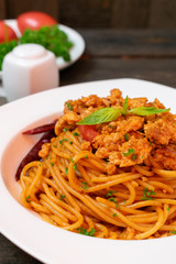 Spicy spaghetti pasta with fried chicken and chili in white dish on black wooden table.