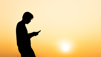 Fototapeta na wymiar Silhouette young man using smartphone during sunset