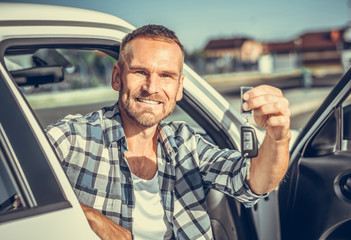 A man in a car shows a key. Buying or renting a car - concept. Toned photo.