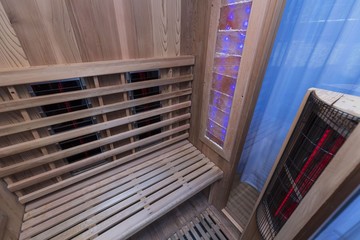 Infrared sauna interior close up view. Wooden walls and bench, ceramic heaters. Healthy lifestyle concept.