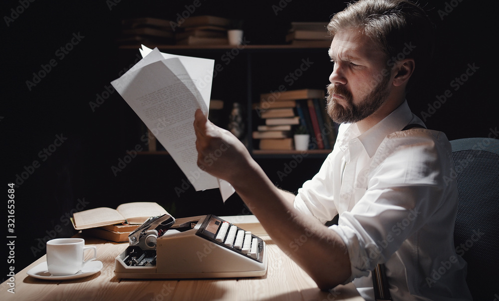 Fototapete writer reading typescript checking his work sitting at ancient typewriter, late night, side view