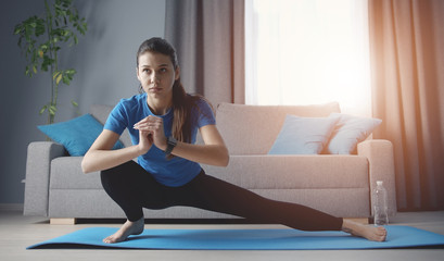 Young concentrated woman doing side lunge yoga position training on roll mat on floor at home - obrazy, fototapety, plakaty