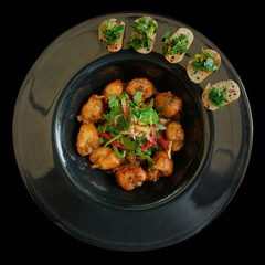 Fried frog legs in black plate on black background
