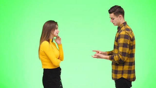 Young woman is argueing with young man, being on green background, isolated. Copy space. 4K.