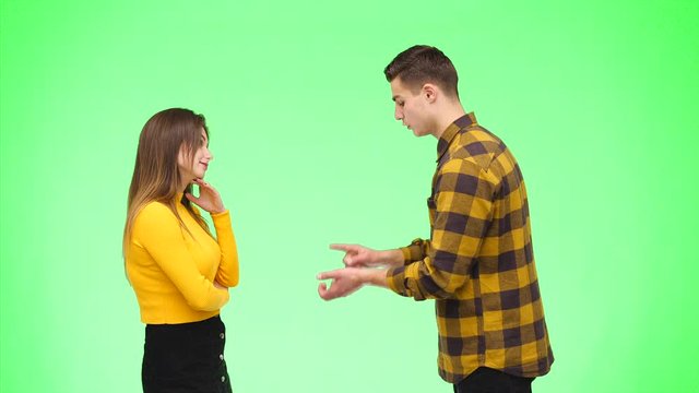 Young woman is argueing with young man, being on green background, isolated. Copy space. 4K.