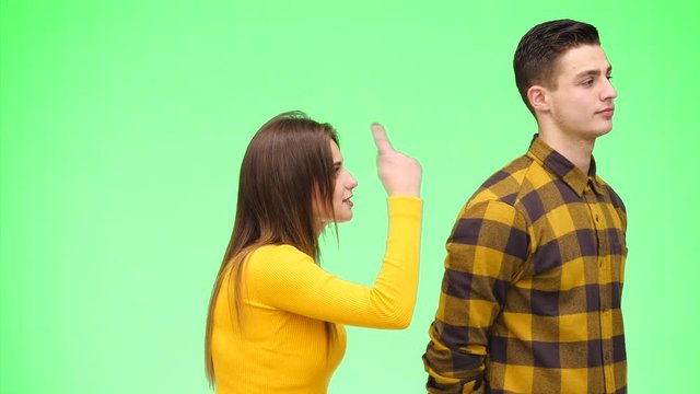 Young woman is argueing with young man, being on green background, isolated. Copy space. 4K.