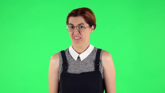 Portrait of funny girl in round glasses is showing disgust for bad smell or taste. Green screen
