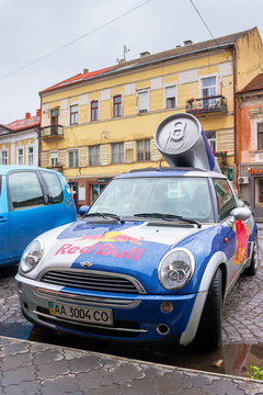 Uzhhorod, ukraine - 14 JUL, 2013: Red Bull mini cooper publicity car with a can of energy drink behind. fancy car tuning used for promotion. wet advertisement vehicle after the rain