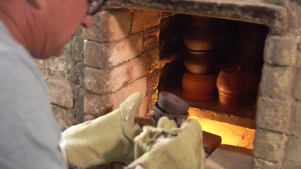 Potter in gloves takes loam items out of brick pottery kiln, close up.