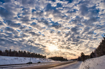 Fototapeta premium Stunning sky in the middle of the wilderness with empty highway. Winter landscape with a motorway going through a forest.