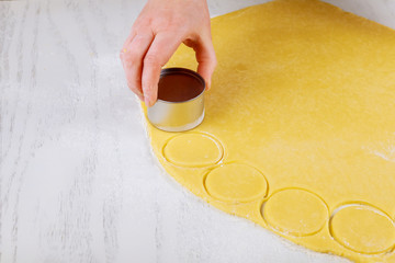 Woman cuts out dough circles for baking cookies on table.