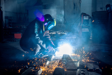 Side view of welder in protective helmet welding metal detail with sparks at factory  