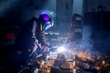 Side view of welder in protective helmet welding metal detail with sparks at factory  