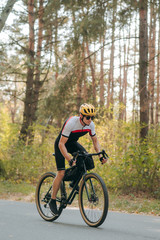Obraz premium Portrait of a man in sports cycling clothes riding on the road in the forest and looking intently into the front. A cyclist rides a bicycle through an autumn forest. Bicycle hobby