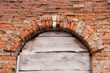 Old red brick masonry and arched window opening clogged with boards. Background for design.