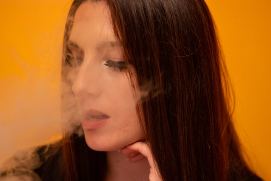 Closeup of a brunette surrounded by smoke. Woman smoking , vaping electronic cigarette. Unhealthy addiction trying to quit