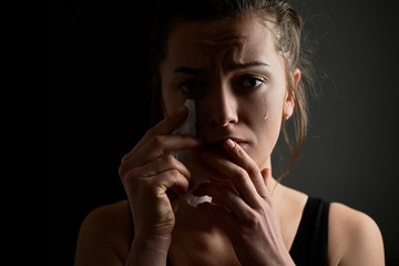 Sad miserable desperate grieving crying woman with tears eyes on a dark black background during trouble, life difficulties, loss and emotional problems