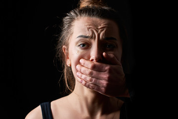 Stressed unhappy scared crying woman victim in fear with closed mouth on a dark black background...