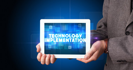 Young business person working on tablet and shows the inscription: TECHNOLOGY IMPLEMENTATION