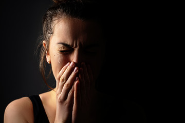 Sad grieving crying female with folded hands and tears eyes on a dark black background during...