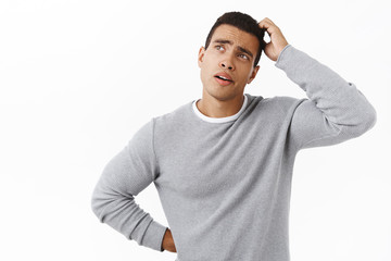 Thoughtful and hesitant good-looking young man, thinking looking focused up, scratching head...