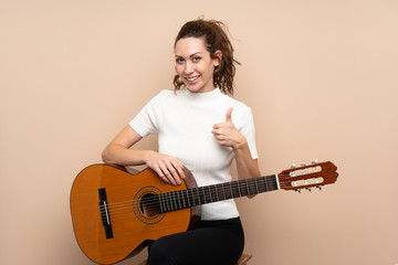 Obraz premium Young woman with guitar over isolated background with thumbs up because something good has happened