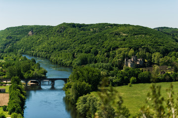 Fototapeta na wymiar View of Dordogne river in Dordogne valley with Castelnaud-la-Chapelle Castle in right side of picture and old stone bridge in summer day. Travel tourist destination Aquitaine, France