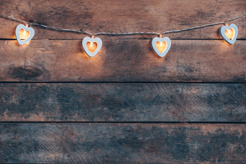 Old wooden background with a garland of white burning hearts. The concept of a Declaration of love, romantic relationships, Valentine's day in grunge style. Copy space.