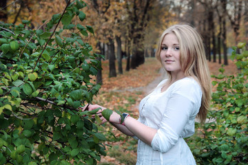 Young blonde girl in autumn in the park near the mock-bush