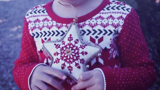 Slow motion. Little girl in red dress holding Christmas ornament on Christmas tree farm.