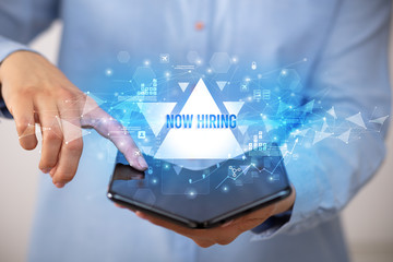 Businessman holding a foldable smartphone with NOW HIRING inscription, business concept