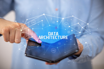 Businessman holding a foldable smartphone with DATA ARCHITECTURE inscription, new technology concept