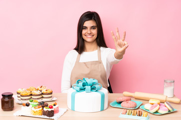Obraz na płótnie Canvas Pastry chef with a big cake in a table over isolated pink background happy and counting three with fingers