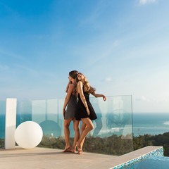 Beautiful girls in an evening dress have fun by the pool with wine and talk about travels and weekends. Discuss March 8th. Leisure and pool parties in a villa by the sea. Thailand, Samui