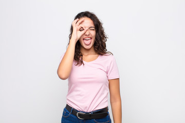 young pretty woman smiling happily with funny face, joking and looking through peephole, spying on...