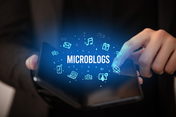 Businessman holding a foldable smartphone with MICROBLOGS inscription, social media concept