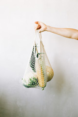 hand holding eco bag with fresh vegetables on white background