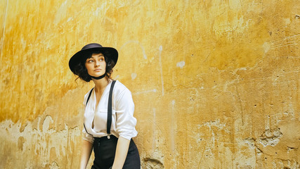 Fototapeta na wymiar A girl in a hat stands by the wall and looks around