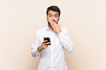 Young man with beard holding a mobile covering mouth with hands